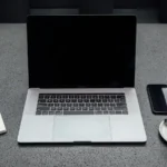 A closed laptop on a desk with a coffee cup, a phone and a notebook